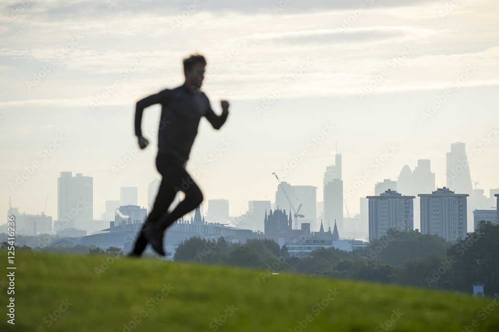 Abstract silhouette of jogger running on the green grass of Primrose Hill in front of the misty London city skyline Abstract silhouette of jogger running on the green grass of Primrose Hill in front of the misty London city skyline