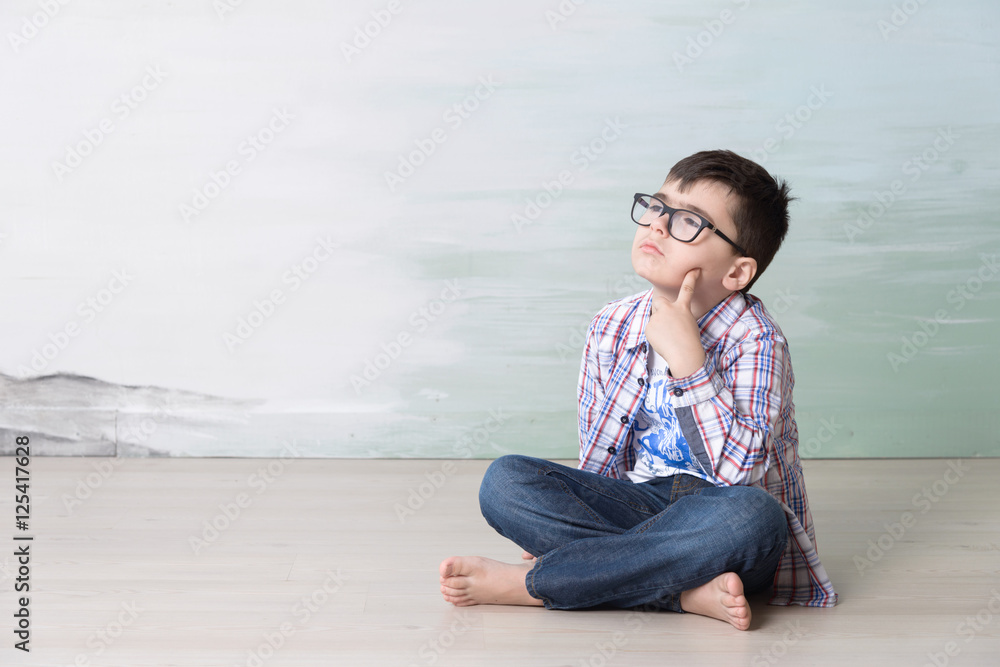 serious little boy sitting on the foor thinking