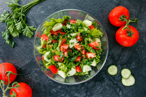 Fresh salad with tomato, cucumber, greens on black background. Top view. Healthy food or diet nutrition concept.