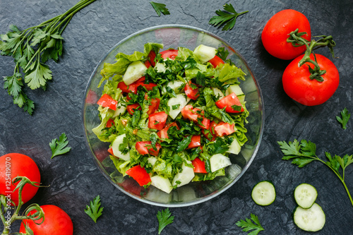 Fresh salad with tomato, cucumber, greens on black background. Top view.