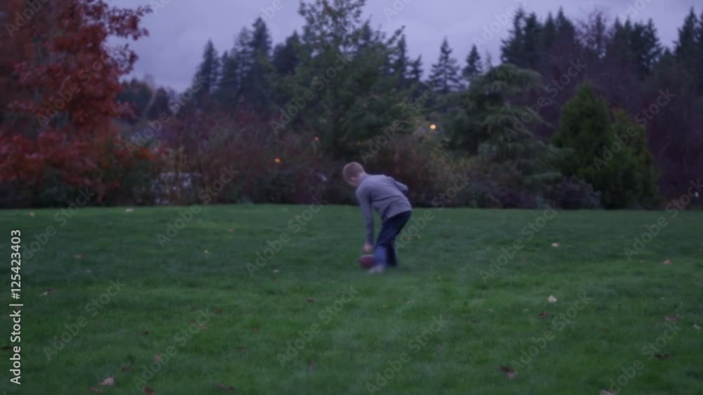 Father and son passing a football in a park at night, slow motion Father and son passing a football in a park at night, slow motion