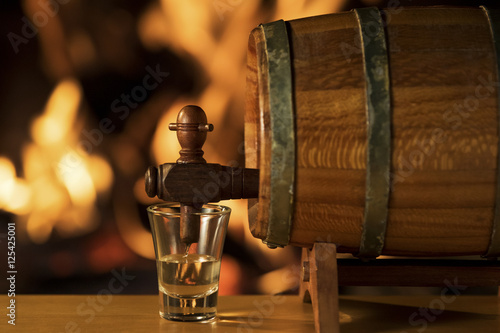 Cachaça Barrel, Brazilian drink / Cachaça being poured into a small glass from a barrel with a fireplace on the background