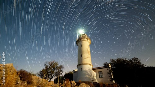 Timelapse of beautiful night landscape with lighthouse with rotating starry sky on a background