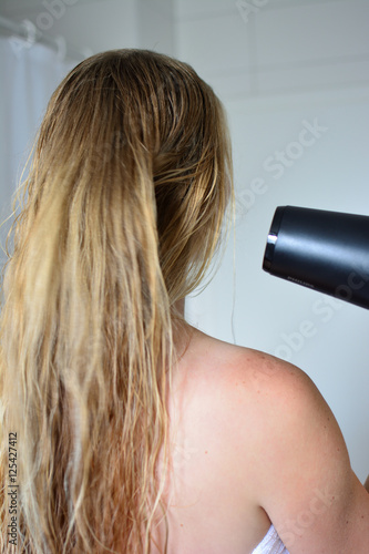 Blond woman drying hair in bathroom