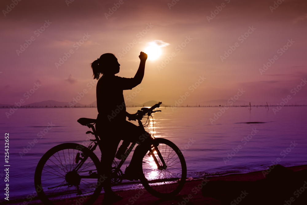 Fototapeta premium Silhouette of happy female celebrating with arm up towards the sun