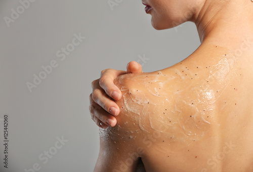Fototapeta Young woman applying scrub on shoulder on grey background