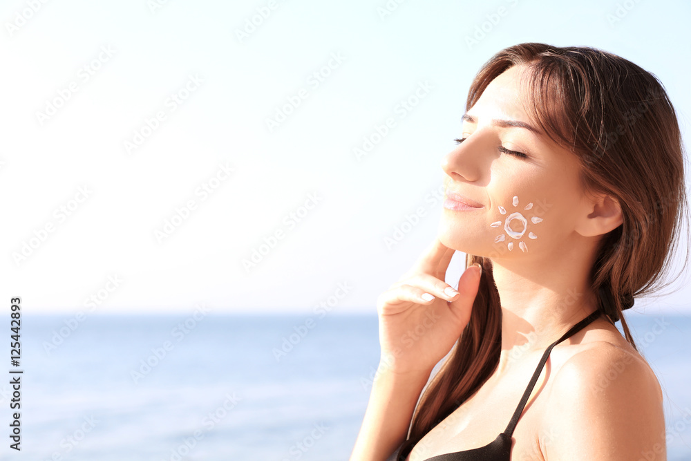 Young woman with sunscreen on face, sea background Young woman with sunscreen on face, sea background