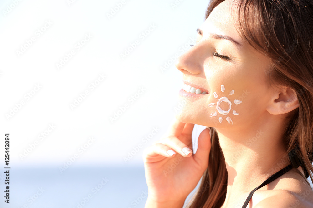 Young woman with sunscreen on face, sea background Young woman with sunscreen on face, sea background