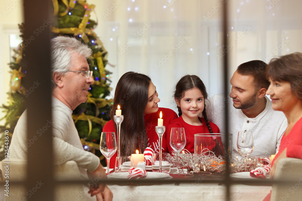 Happy family sitting at table served for Christmas dinner, view from window Happy family sitting at table served for Christmas dinner, view from window