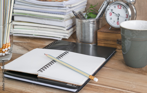 Office table with blank notebook, clock, coffee cup. photo