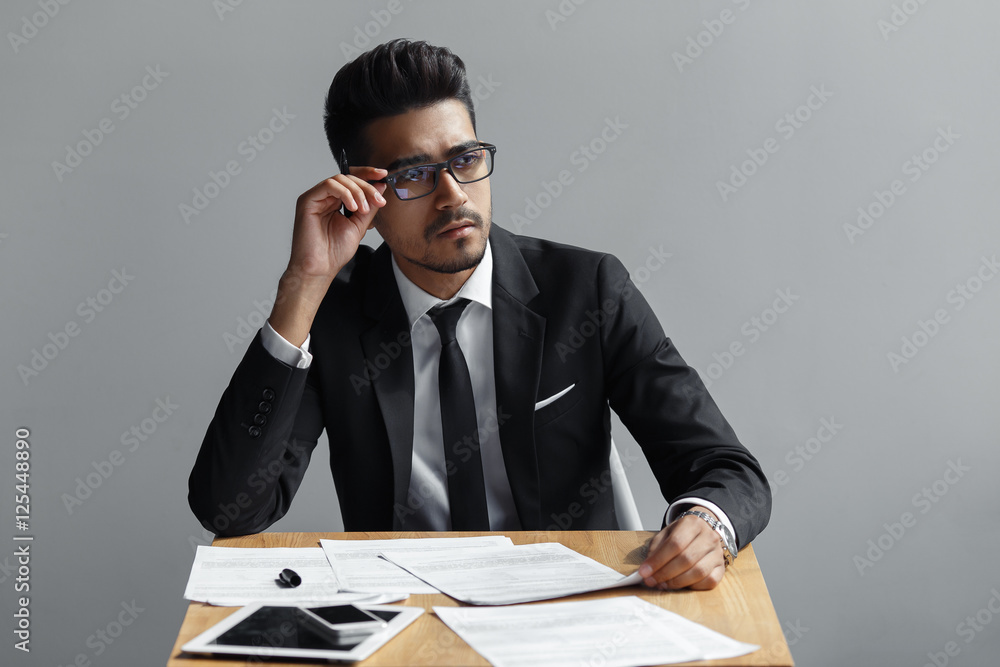 successful man with glasses looking away from the camera, the tablet, telephone and papers on the table. successful man with glasses looking away from the camera, the tablet, telephone and papers on the table.