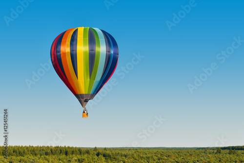 Aerial view of a multicolored hot air balloon flying over a forest
