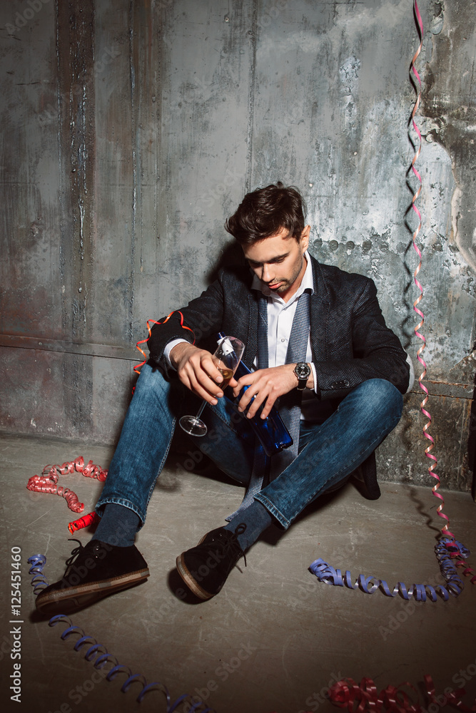 Drunk man sitting on the floor with alcohol at christmas after party. Hangover, overdrunk concept