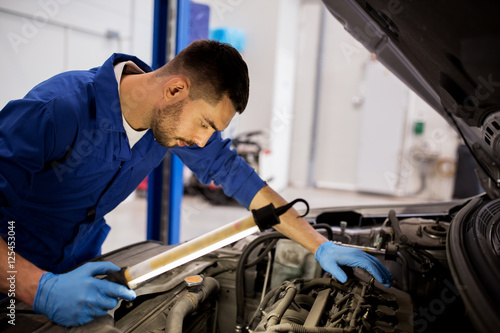 mechanic man with lamp repairing car at workshop