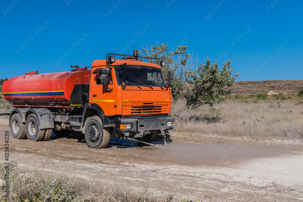 Big orange street cleansing machine washes the dusty road