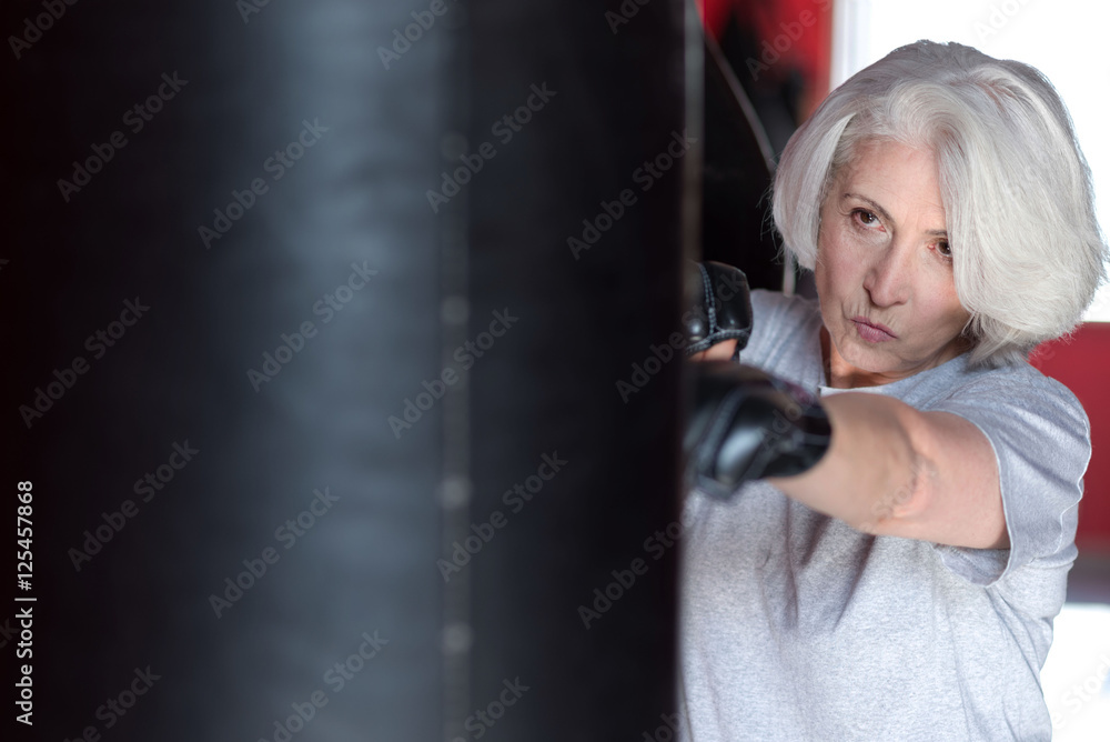 Close up of senior concentrated woman boxing punching bag.