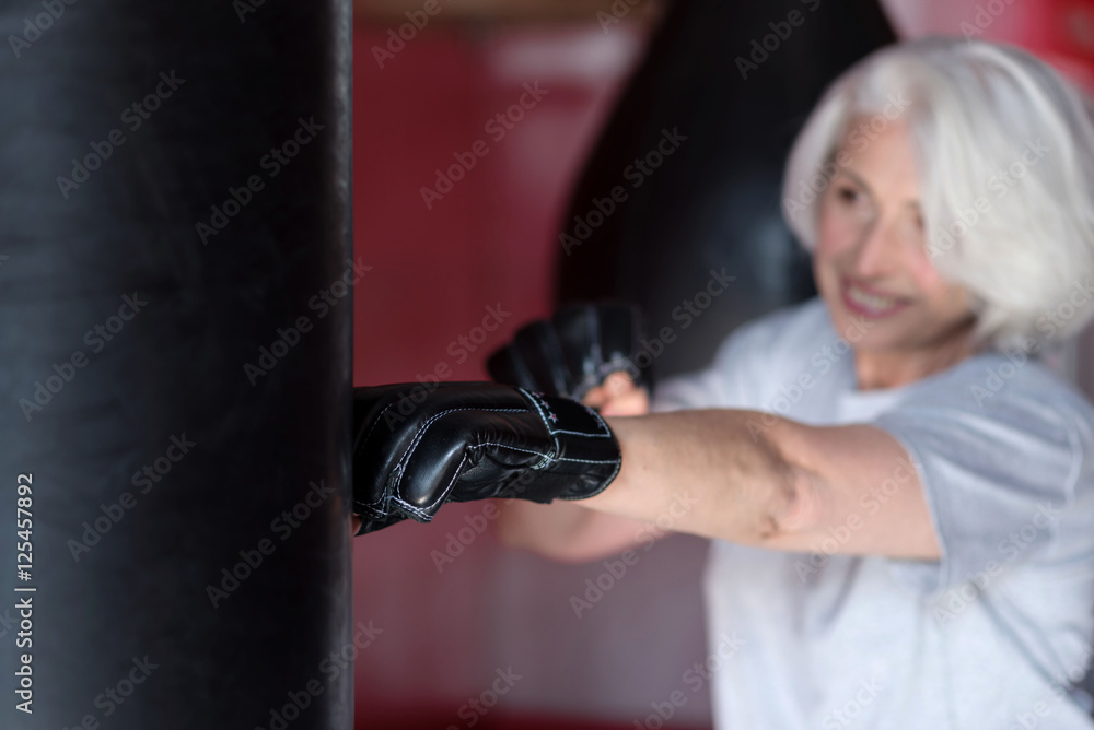 Motivated smiling senior woman boxing punching bag.