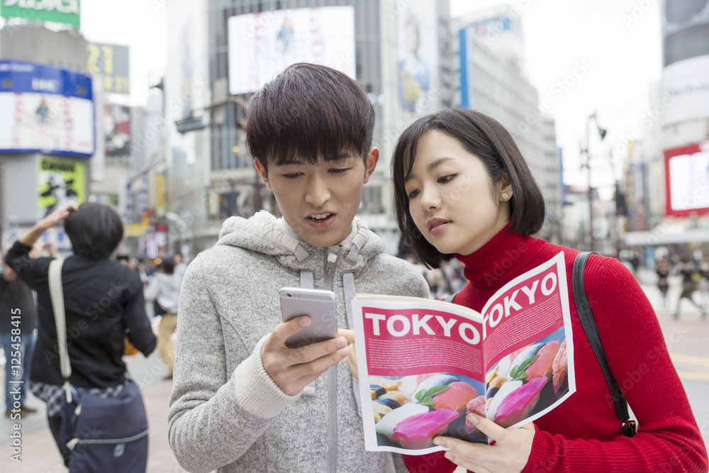 Obraz premium カップル 男女 東京観光 デート 渋谷スクランブル交差点 ガイドブックを手に スマホで検索