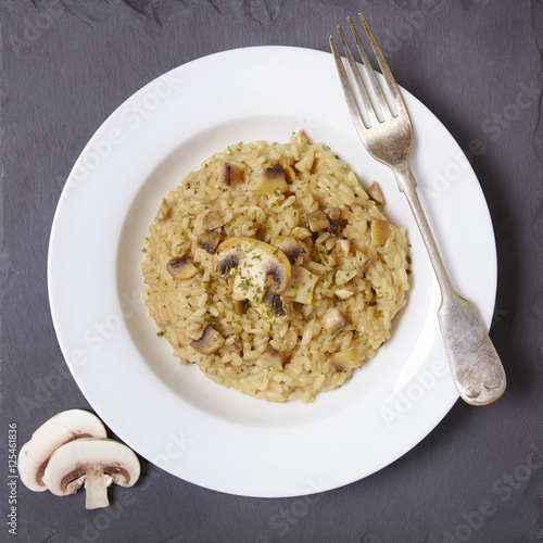 Aerial view of a dinner plate of chicken and mushroom risotto rice on a rustic slate background