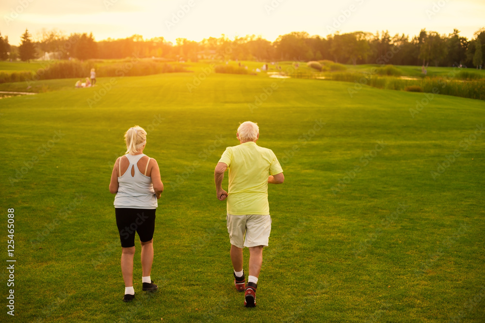 Back view of jogging couple. Elderly people in sport clothes. Morning starts from exercising. Remain healthy and active.