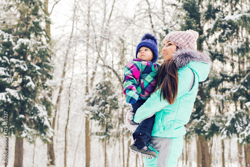 Mother and little toddler girl walking in the winter forest and having fun with snow. Family enjoying winter. Christmas and lifestyle concept.