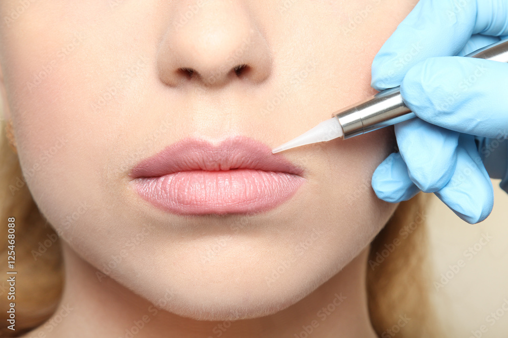 Cosmetologist making permanent  make up on lips, close up