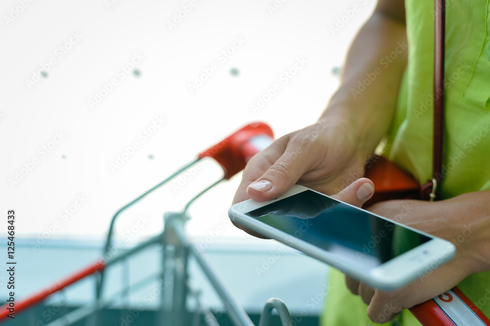 Closeup on person holding smartphone in hand during shopping. Cart on indoor store window background Closeup on person holding smartphone in hand during shopping. Cart on indoor store window background