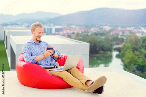 Freelance businessman. Young handsome man working on laptop while sitting on the roof top.