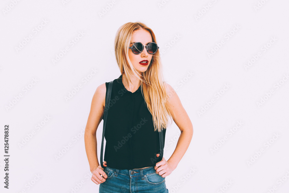 beautiful young blond girl standing against white wall,wearing jeans,black top with black backpack smiling snow-white smile with red lips,wearing glasses and looking away,perfect advertising photo beautiful young blond girl standing against white wall,wearing jeans,black top with black backpack smiling snow-white smile with red lips,wearing glasses and looking away,perfect advertising photo