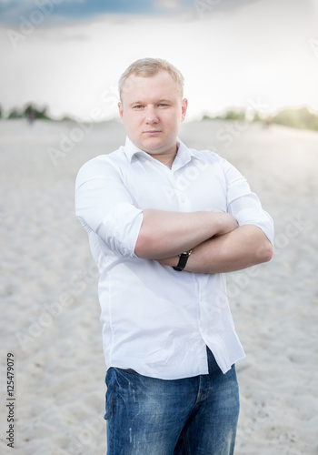 Portrait of handsome man in jeans and white shirt posing on sand