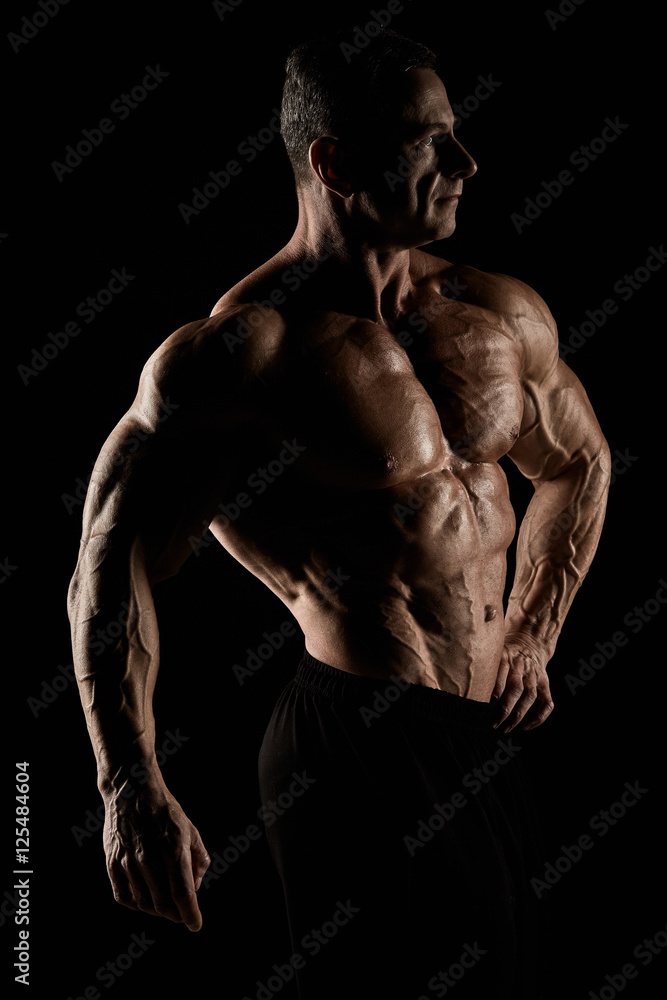 Fototapeta premium torso of attractive male body builder on black background.