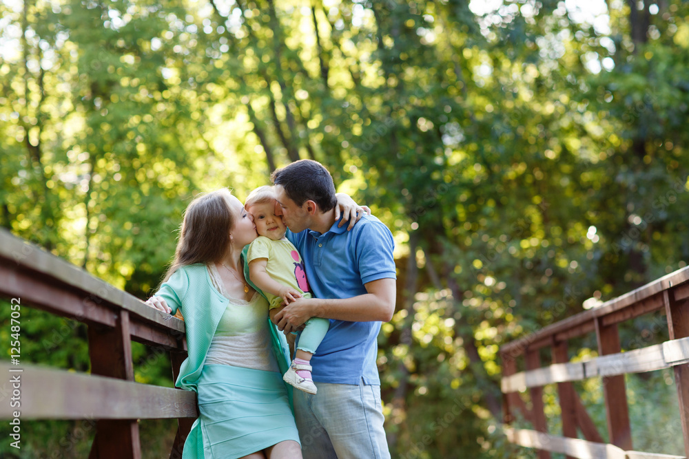 Family portrait outdoors of mom and dad kissing their daughter Family portrait outdoors of mom and dad kissing their daughter