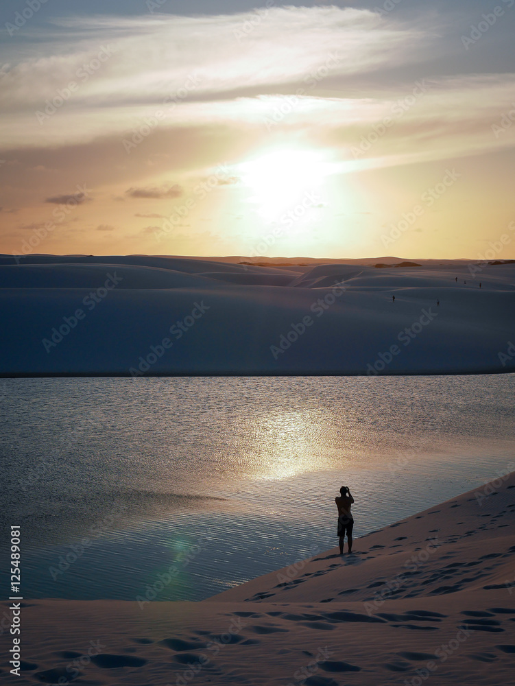 Fototapeta premium A solitary man enjoying a moment alone among the lagoons and sand dunes of the Lençóis Maranhenses National Park - Barreirinhas, Maranhão, Brazil.