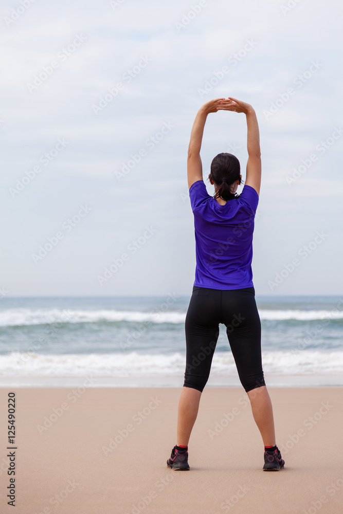 Female athlete warming up and stretching the upper body before running at the beach on an Autumn day. Female athlete warming up and stretching the upper body before running at the beach on an Autumn day.