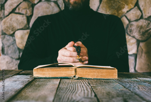 Photo a man in black clothes with a prayer beads in hand praying in front of an old open book