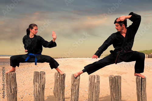 Two martial arts fighters practicing combat sport on the beach poles: man and woman doing a Karate - Viet Vo Dao posture