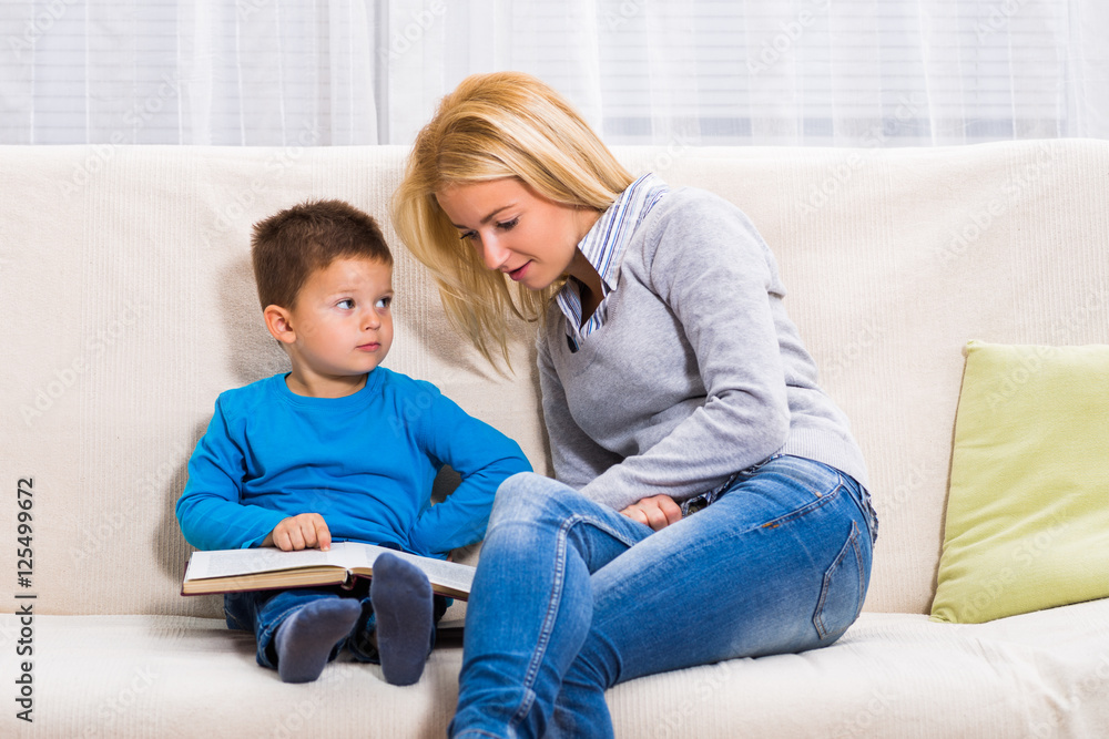 Happy mother and son are sitting on sofa and reading book together. Happy mother and son are sitting on sofa and reading book together.