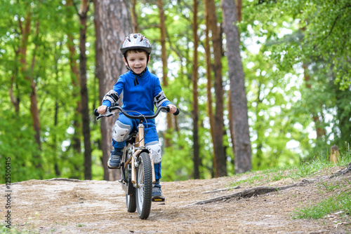 Happy funny little kid boy in colorful raincoat riding his first bike on cold day in forest. Active leisure for children outdoors. carefree childhood concept © pahis