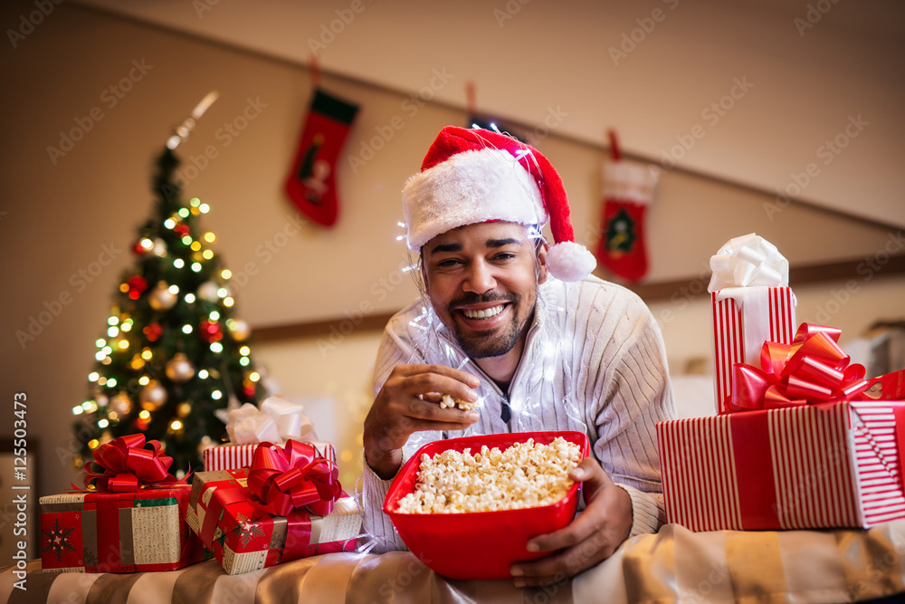 Smiling young man laying on bed with popcorns in his hands.