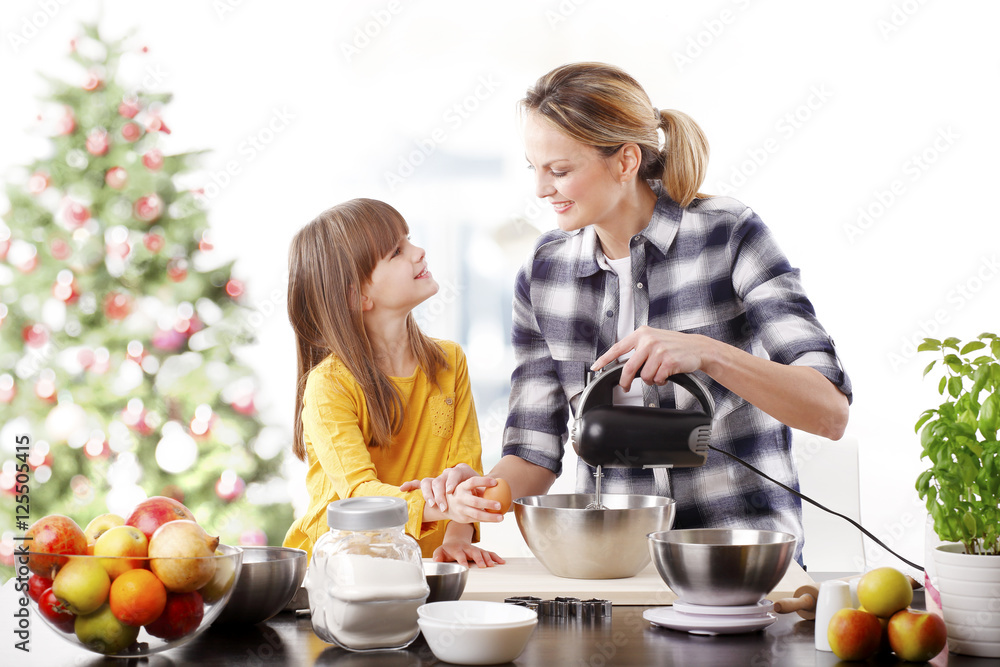 Mother and daughter at christmas.Portrait of cute daughter and her mom baking christmas cookies together in the kitchen. Mother and daughter at christmas.Portrait of cute daughter and her mom baking christmas cookies together in the kitchen.