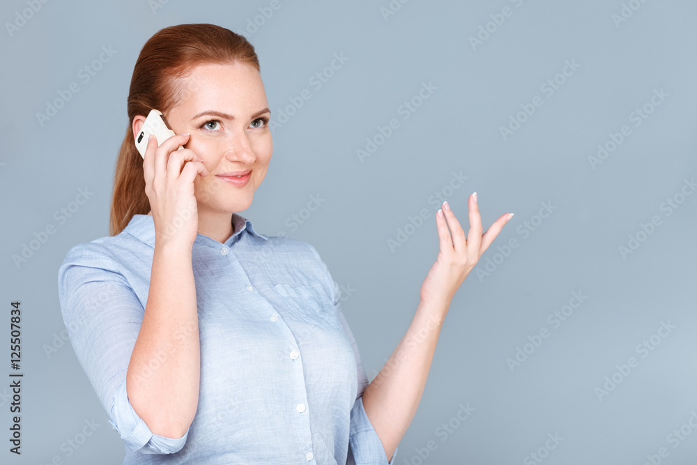 Business talk. Confident young woman talking on the mobile phone and gesturing while standing against grey background Business talk. Confident young woman talking on the mobile phone and gesturing while standing against grey background