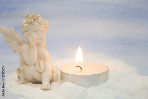 white angel figurine and candle on a pale blue background