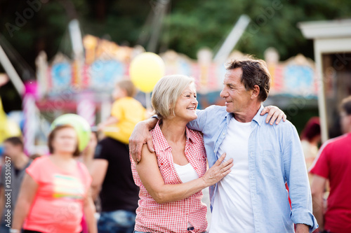 Senior couple at the fun fair, hugging. Sunny summer.