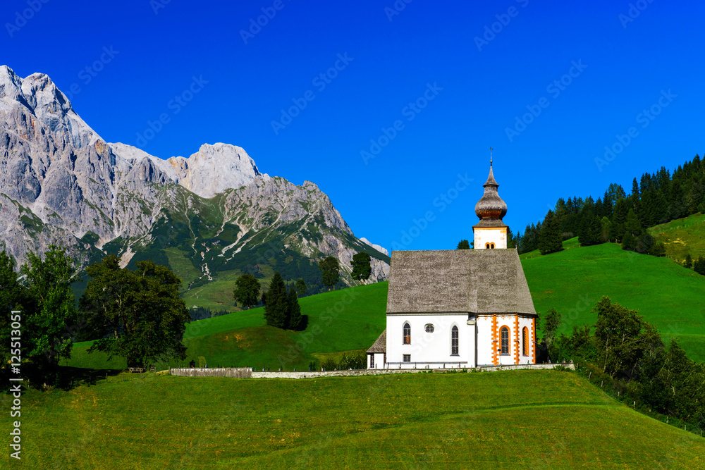 Beautiful little church in Alps. Sunny day, green grass on the h
