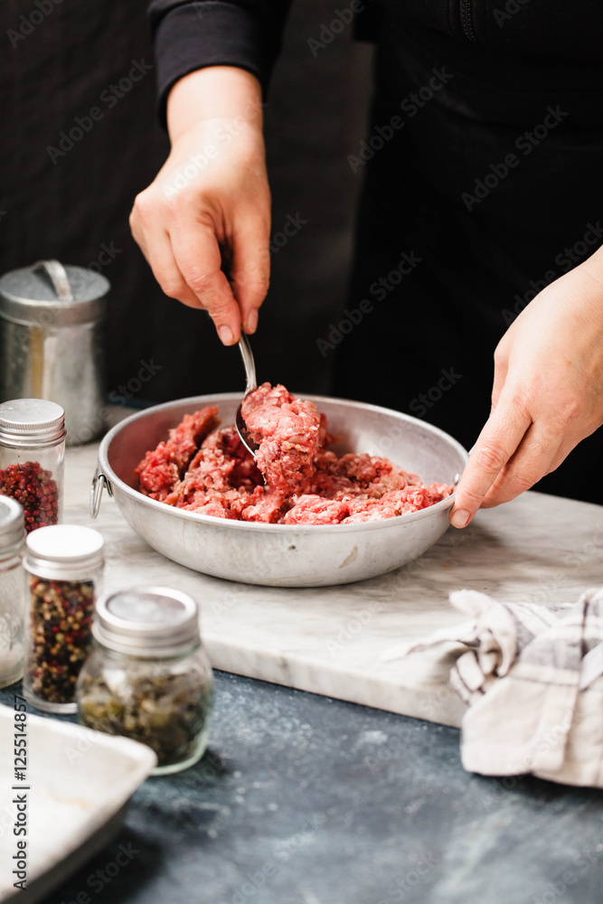 Seasoning Minced Beef In A Bowl. Female chef hands mixing minced meet in a bowl on a kitchen table. Low key