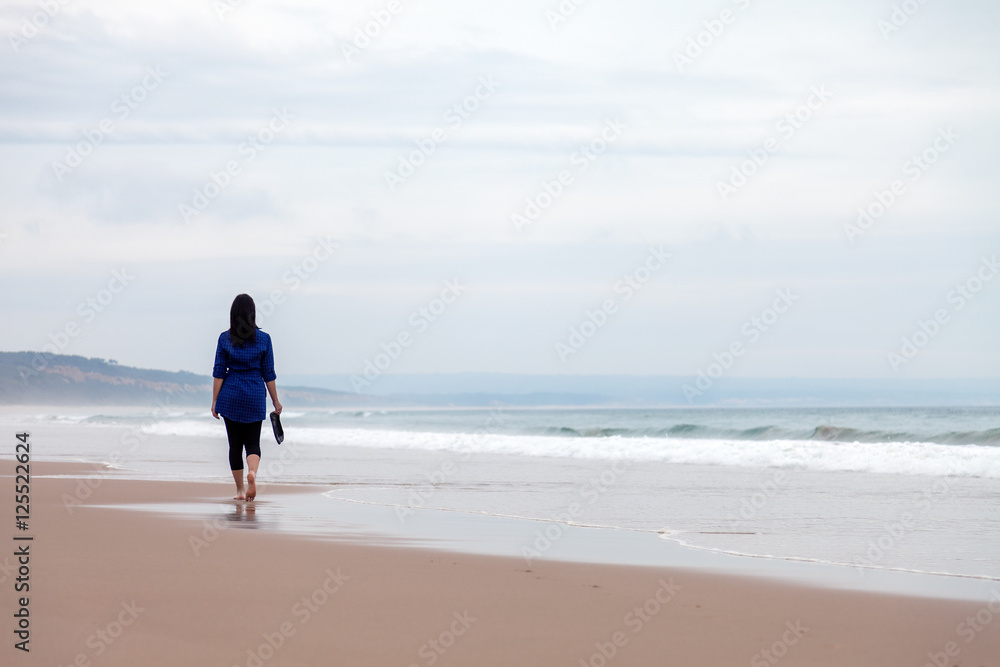 Young woman walking away alone in a deserted beach on an Autumn day. Young woman walking away alone in a deserted beach on an Autumn day.