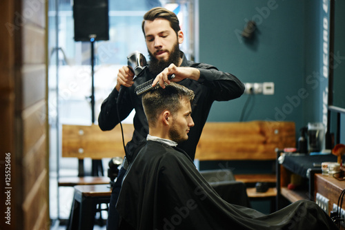 The Barber man in the process of drying a client's hair with a Hairdryer at the hairdresser photo