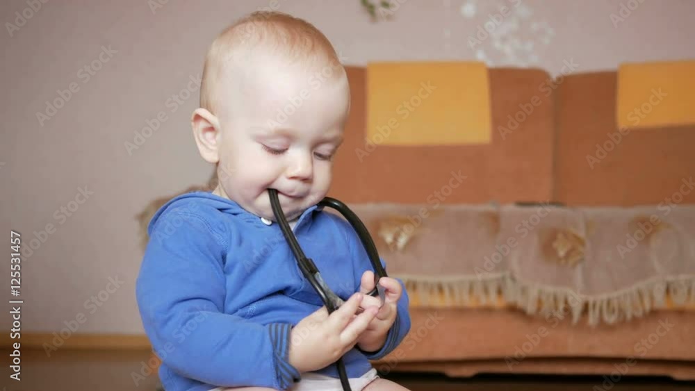 Sweet baby with stethoscope at home. Toddler chews medical device teeth Sweet baby with stethoscope at home. Toddler chews medical device teeth