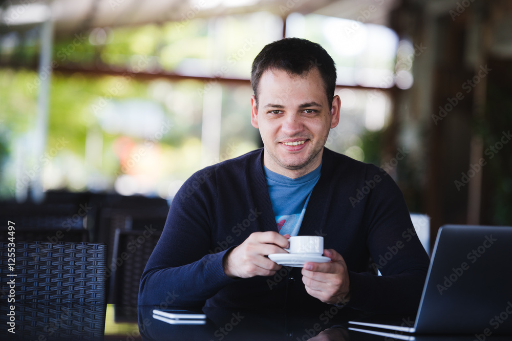 Handsome young man working on laptop and smiling while enjoying coffee in cafe Handsome young man working on laptop and smiling while enjoying coffee in cafe