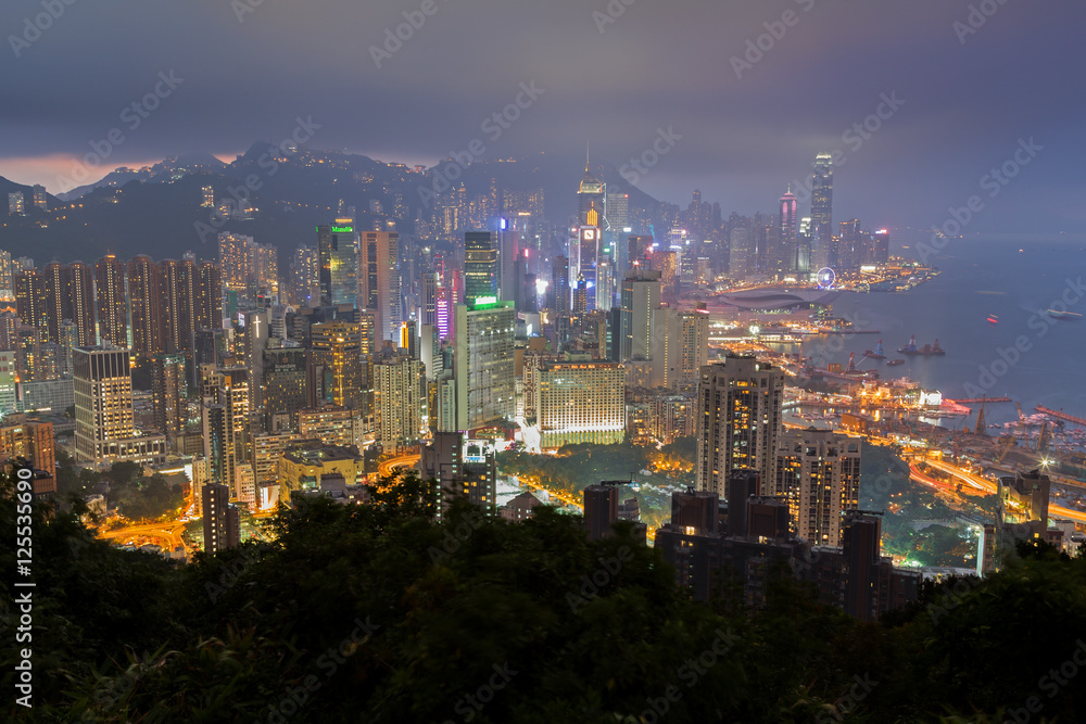 Fototapeta premium Oświetlone wieżowce na wyspie Hongkong w Hongkongu, Chiny, oglądane ze wzgórza Braemar w mglisty i pochmurny wieczór.